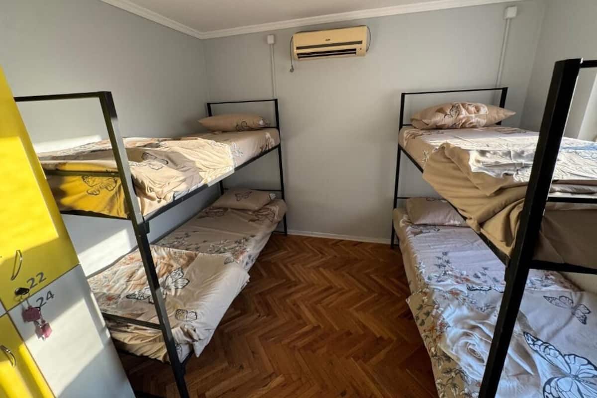 Una habitación con literas, suelo de madera y un equipo de aire acondicionado en la pared.