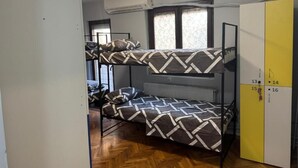 Una habitació de dormitori amb lliteres, un radiador, un armari i una finestra amb cortines estampades.