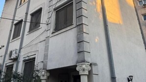 Un edifici de diversos pisos amb entrada al cantó, grans finestres i un balcó amb baranes.