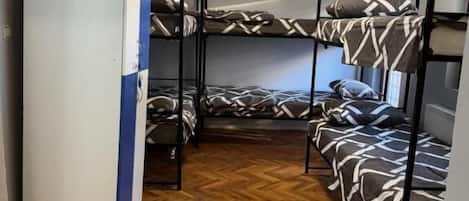 A dormitory room with bunk beds, a wooden herringbone floor, and an air conditioning unit.