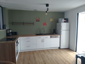 Une cuisine avec des meubles blancs, un plan de travail en bois, une machine à café, un réfrigérateur et un luminaire suspendu.