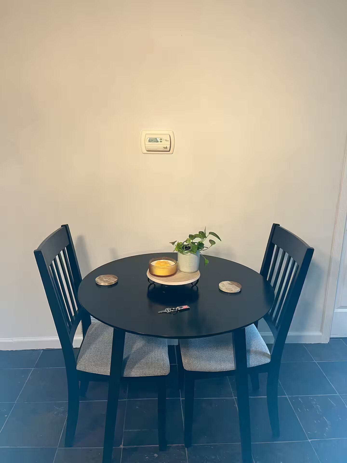A round dining table with four chairs, a potted plant, and a candle on the table.
