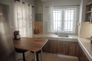 A kitchen with a wooden table, a coffee maker, and a window with a view. - No. 17 - The Grand Gaube Retreat – Pool, Turquoise Sea Just Steps Away (Grand Gaube)