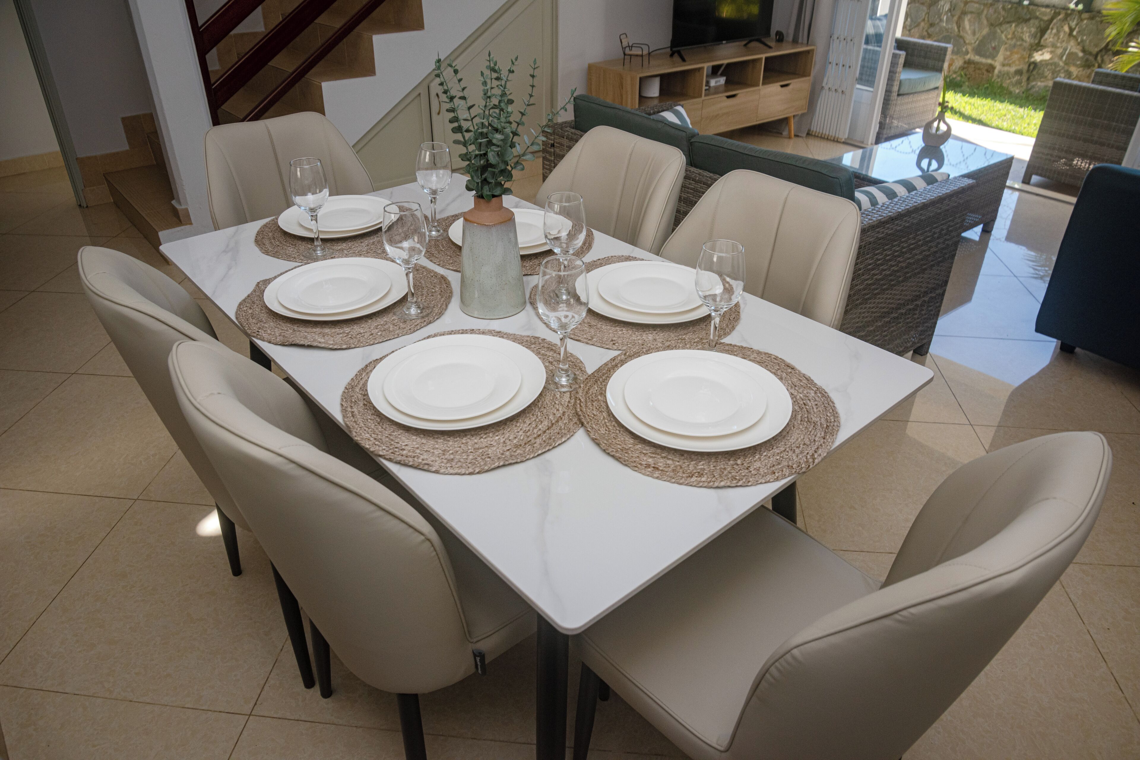 A dining table set with white plates, clear glasses, and woven placemats.
