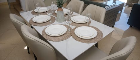 Une table à manger dressée avec de l’assiette blanche, des verres transparents et des sets de table en fibres tressées.
