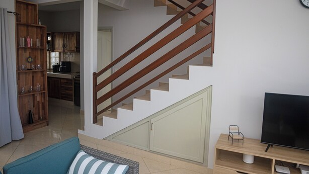 A staircase leading to a second floor, a dining area with wooden cabinets, a television on a wooden stand, and a sofa with a striped cushion. - No. 17 - The Grand Gaube Retreat – Pool, Turquoise Sea Just Steps Away (Grand Gaube)