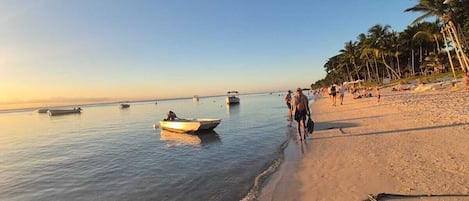 A beach with clear skies, calm water, and a few boats.
