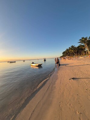 Uma praia com céu claro, águas calmas e alguns barcos.