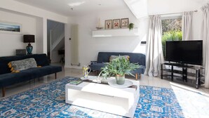 A modern living room with a sofa, TV, coffee table, and a staircase. - West Wittering Beach House Garden Parking (Chichester)
