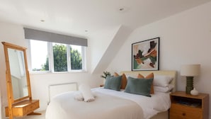 A bedroom with a large bed, a bedside table, a nightstand, a mirror, and a window. - West Wittering Beach House Garden Parking (Chichester)