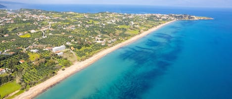 An aerial view of a coastal area with a beach, residential buildings, and greenery.