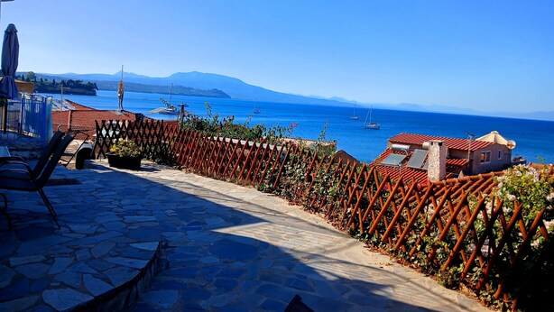 A stone-paved patio with a view of the sea and boats, a red fence, and a building with a red roof. - Angira 4 Seaview Escape - Koroni Summer Getaway (Pylos-Nestoras)