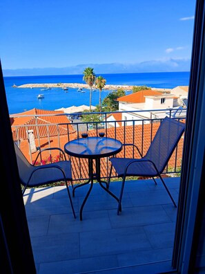 A balcony with a table and chairs, overlooking a coastal area with boats and buildings. - Angira 3 Seaview Escape - Koroni Sunny Getaway (Pylos-Nestoras)