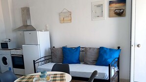 Ett kompakt bostadsutrymme med ett litet kök, en soffa med blå kuddar, ett matbord med stolar och ett klinkergolv.