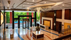 A hotel lobby with a reception desk, a turnstile, a fireplace, and a staircase. - Bel La Monde Blu Chhattarpur (New Delhi)