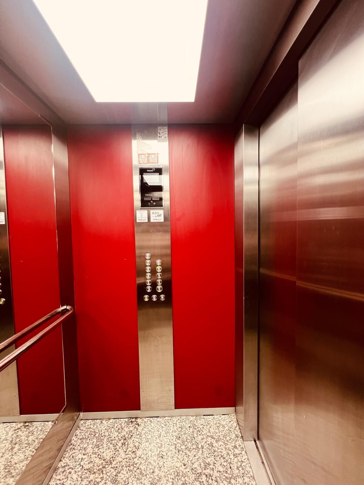 An elevator with red walls and a metallic interior, featuring a control panel with buttons and a display.