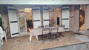 Eine überdachte Terrasse mit Tisch und Stühlen, einer Glasschiebetür und einem gefliesten Boden.