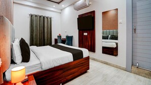 A hotel room with a bed, a desk, a chair, an air conditioning unit, a television, and a door. - Collection O Kotdwar Railway Junction (Kotdwāra)