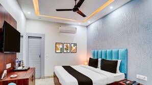 A modern bedroom with a bed, bedside tables, a desk, a ceiling fan, an air conditioning unit, and framed artwork on the wall. - Collection O Kotdwar Railway Junction (Kotdwāra)