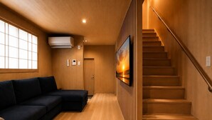 Ein modernes Interieur mit einer Holztreppe, einem dunklen Sofa und einem an der Wand befestigten Fernseher.