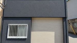 Ein modernes Gebäude mit einer Garagentür, einem kleinen Fenster mit Gitterstäben und einem vergitterten Fenster.