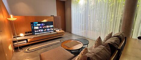 Moderni olohuone, jossa on litteänäyttöinen televisio, sohva, sohvapöytä ja lattiavalaisin.