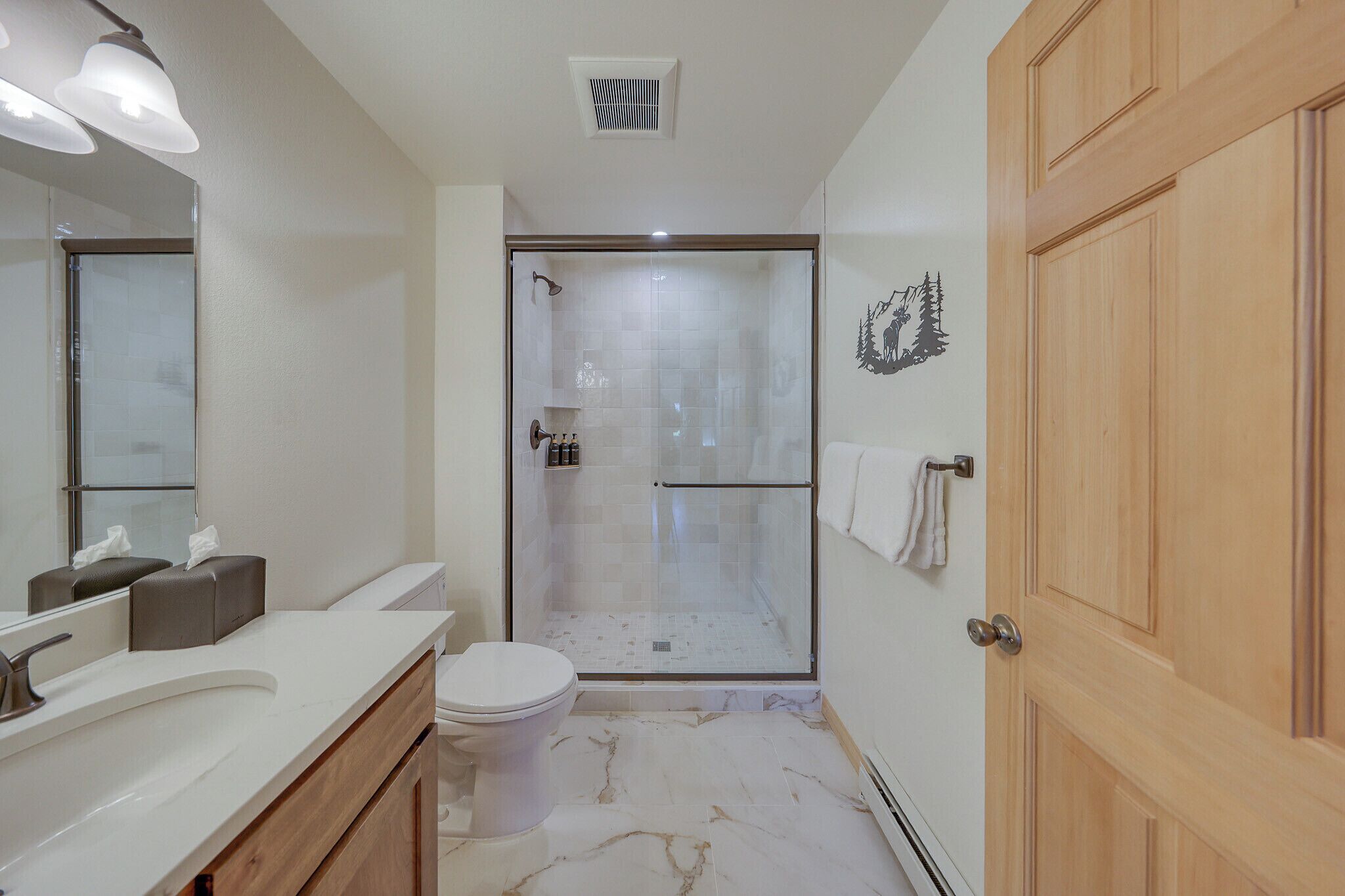 A modern bathroom with a glass-enclosed shower, a toilet, and a vanity with a mirror.
