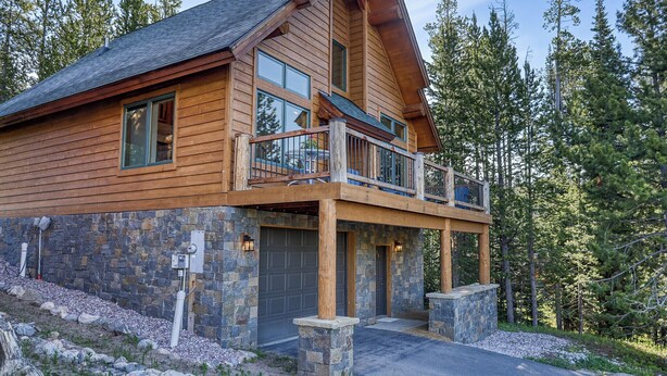 Une cabane en rondins avec des fondations en pierre, de grandes fenêtres et un balcon.
