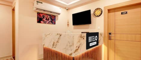 A hotel reception desk with a marble top, a clock, and a TV mounted on the wall.