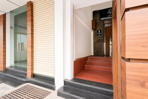 A hotel reception area with a reception desk, a staircase leading to the first floor, and a glass door to the left.