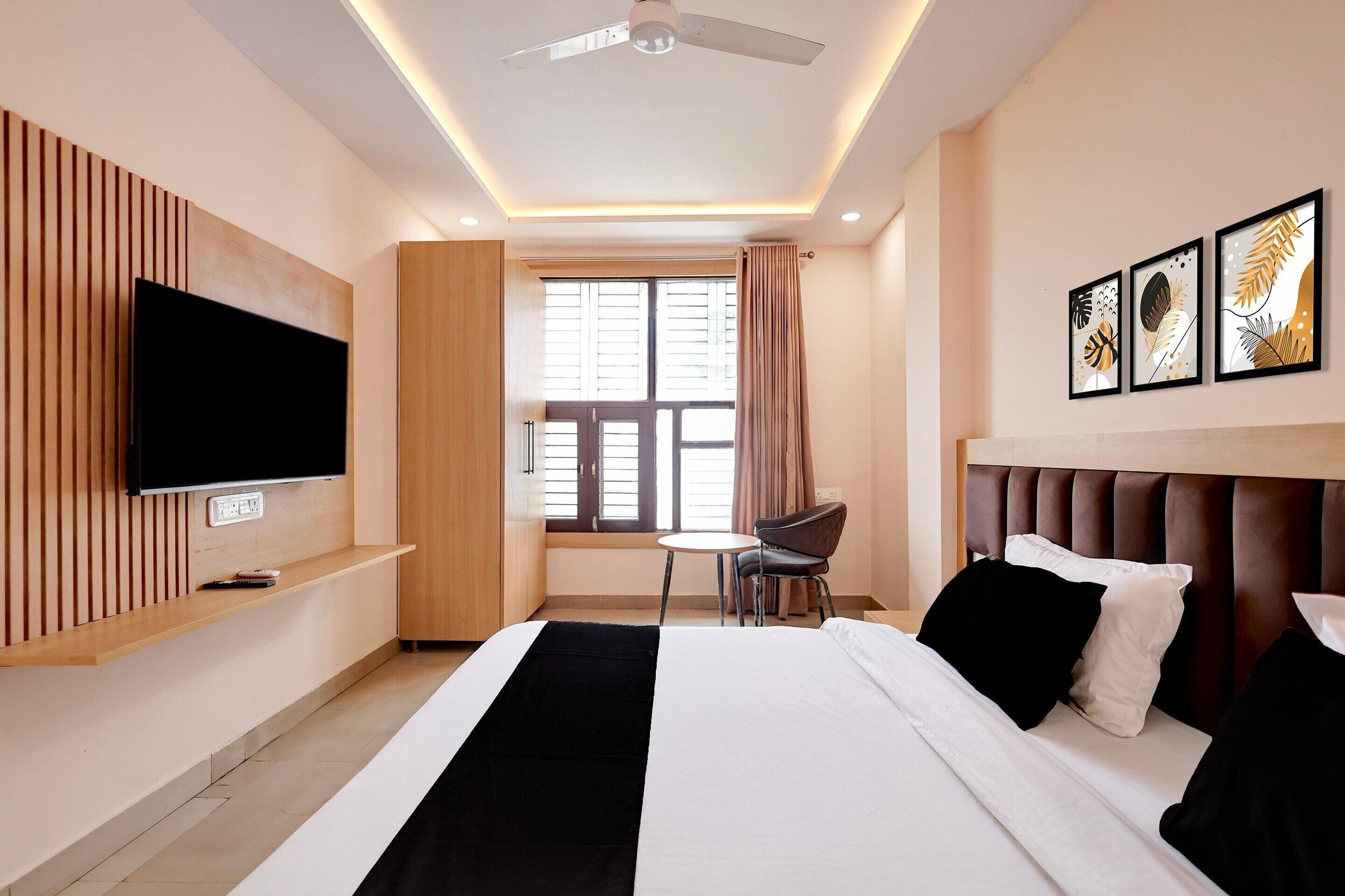 A hotel room with a bed, a TV, a desk, and a window with curtains.
