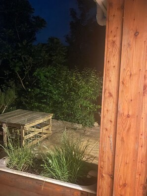 Eine Holzterrasse mit rustikalem Tisch und Bänken, umgeben von üppigem Grün und einer Steinmauer.