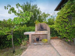 A brick outdoor grill with a chimney, surrounded by greenery and a paved patio. - Rio del sole by Interhome (Montescudaio)