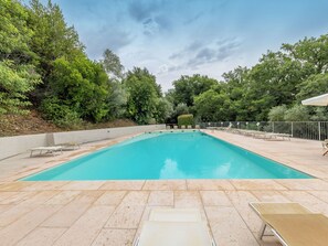 A rectangular swimming pool with a tiled deck, surrounded by trees and a metal fence. - Rio del sole by Interhome (Montescudaio)