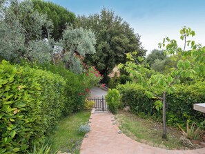 A garden pathway leading to a building, surrounded by various types of greenery and trees. - Rio del sole by Interhome (Montescudaio)