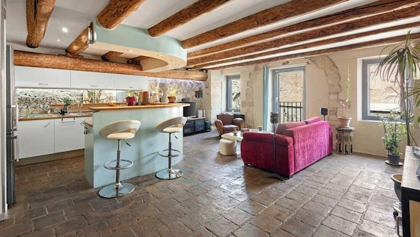 A spacious interior with exposed wooden beams, a kitchen area, a seating area with a red sofa, and a bar with stools.