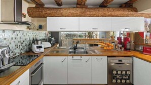 A modern kitchen with wooden beams, white cabinets, a stainless steel sink, and a coffee machine.