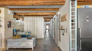 A narrow hallway with a stone floor, wooden beams on the ceiling, a refrigerator on the right, and a motorcycle on the left.