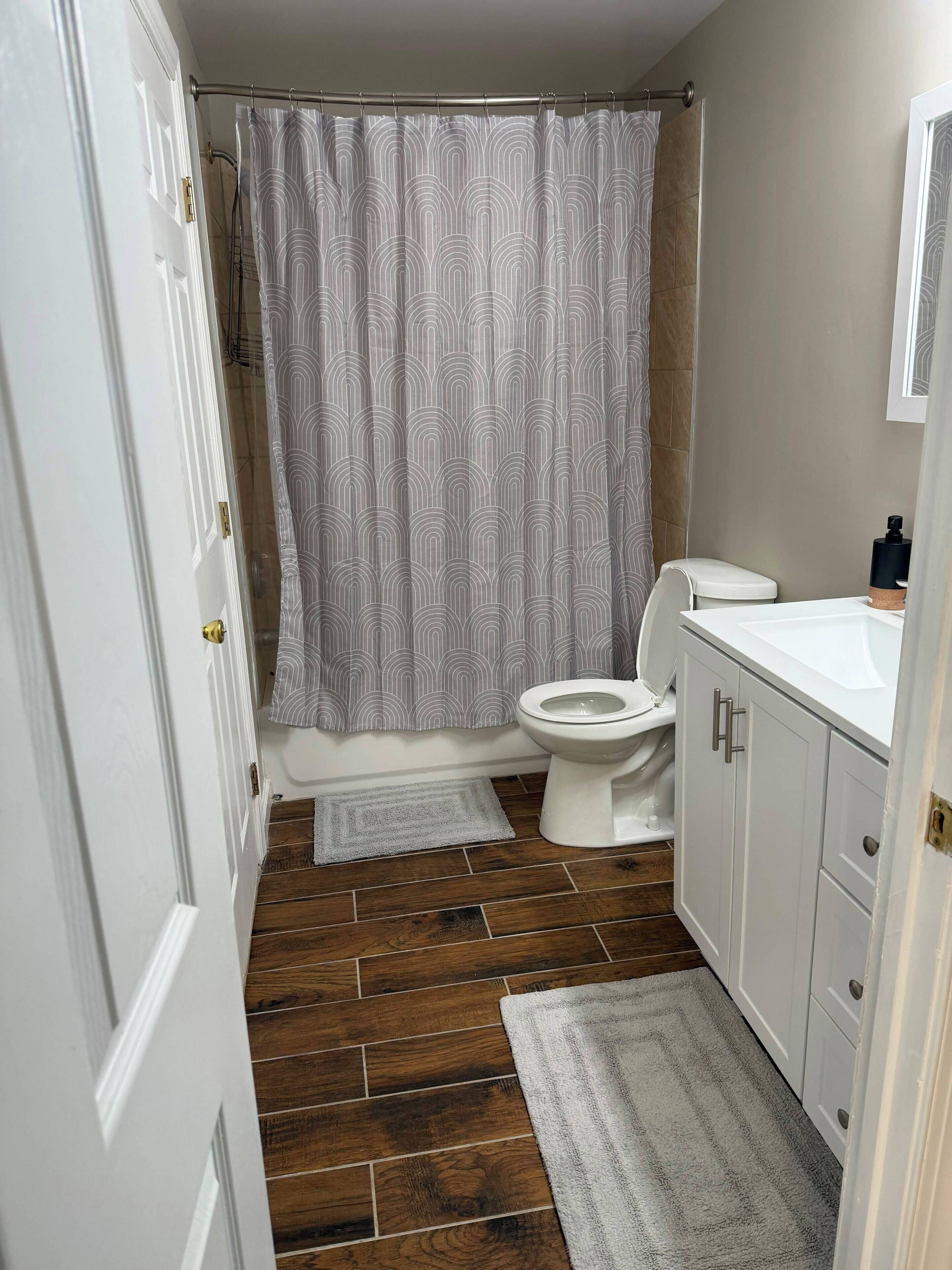 Un baño con cortina de ducha, inodoro, lavabo y suelo de madera.