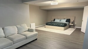 A modern bedroom with a sofa, a bed with a patterned bedspread, and a white rug.