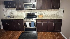 A kitchen with dark cabinets, a stainless steel microwave, a stove, and a sink.