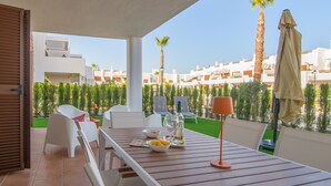 Una terrassa amb taula preparada per dinar, cadires exteriors, una ampolla i un bol de fruita.
