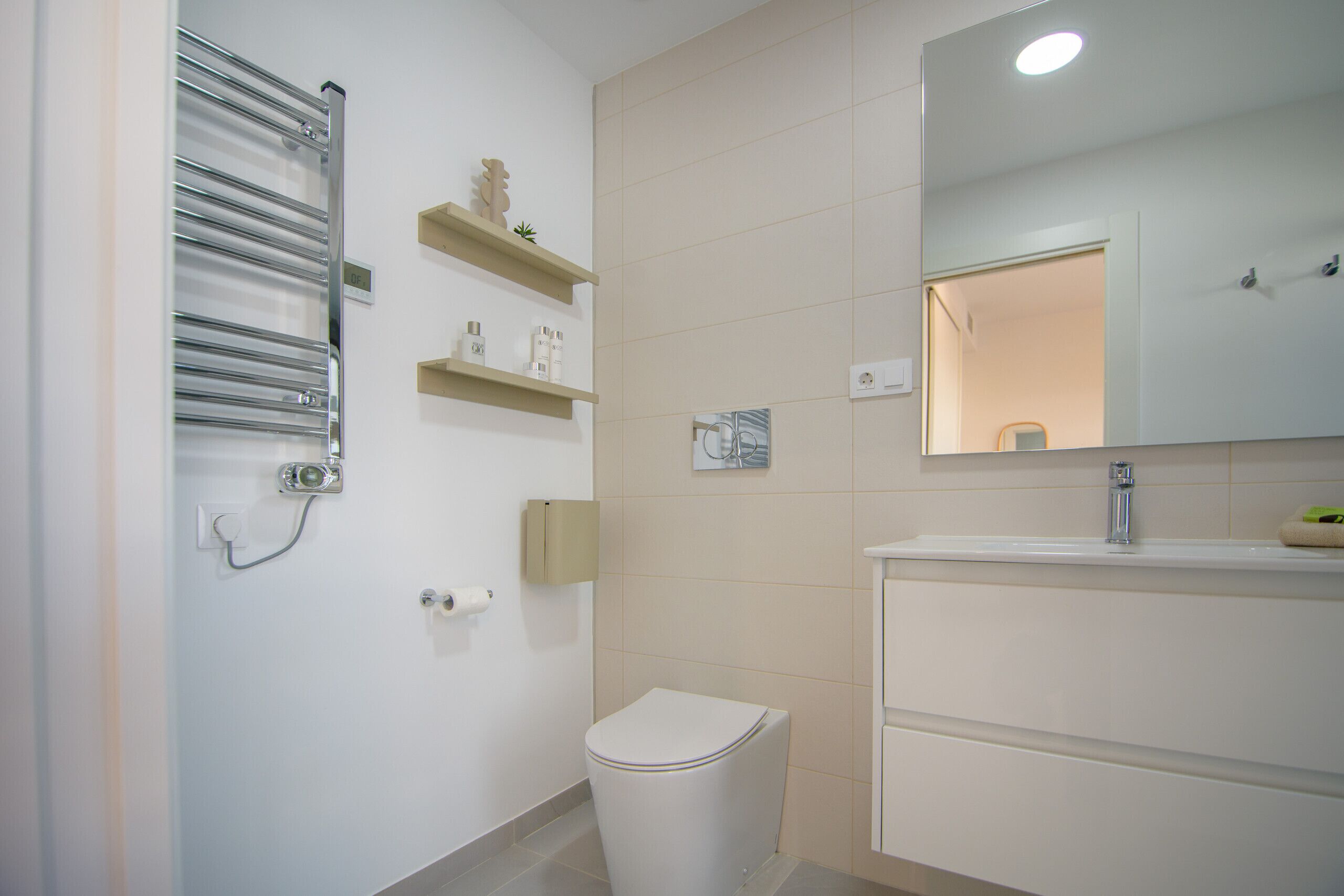 Un baño con inodoro, lavamanos, espejo y toallero.
