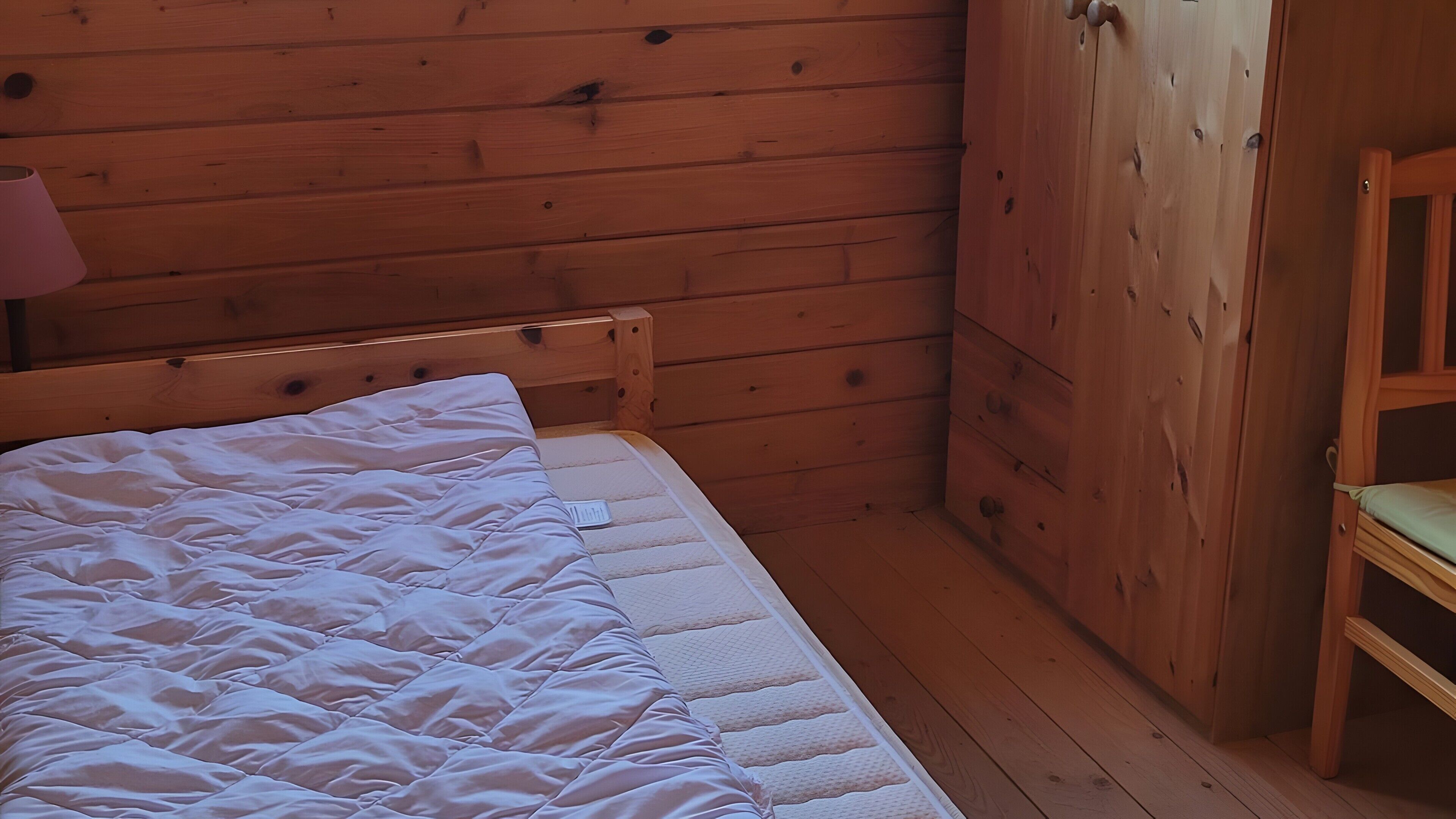 Een houten kamer met een bed, een stoel en een houten kledingkast.