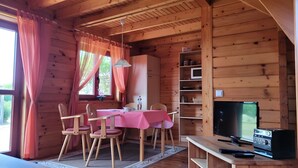 A wooden cabin with a dining area, a television, and a shelf with various items.