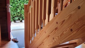 A wooden staircase with a handrail, leading to an outdoor area with greenery.