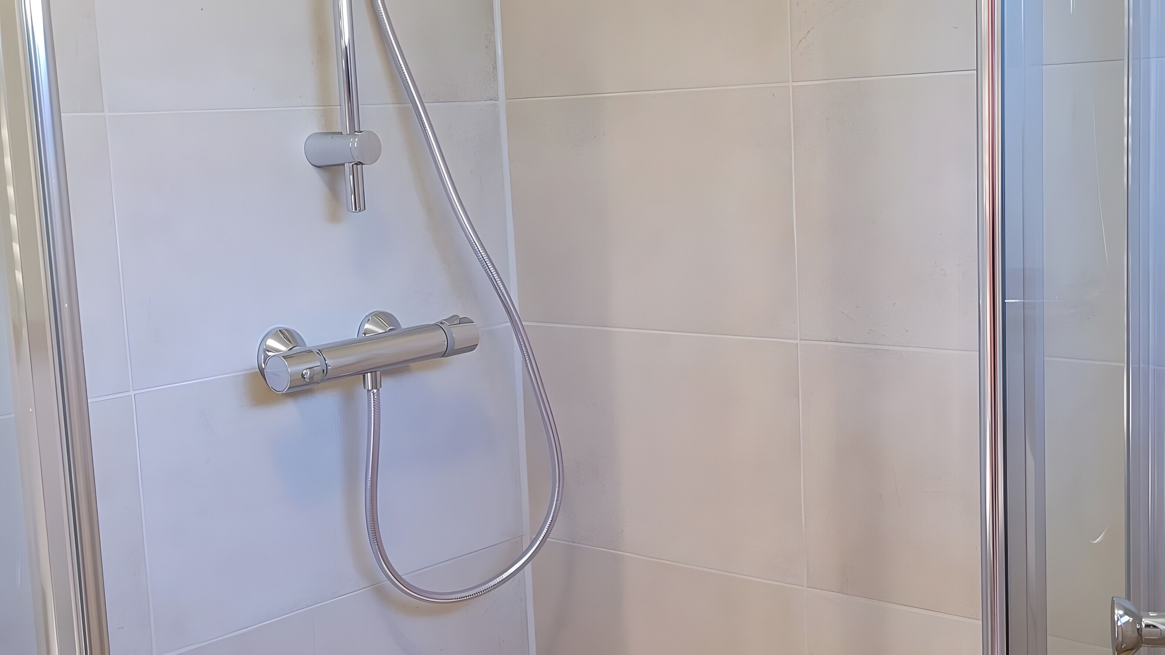 Une douche équipée d’un flexible et d’une commande fixée au mur.