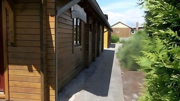 A narrow pathway flanked by wooden buildings with large windows and a small garden area.