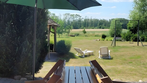 Terassialue, jossa on puinen penkki, kaksi aurinkotuolia ja pergola.