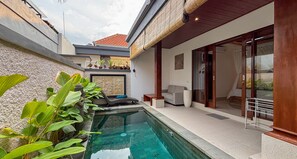 A swimming pool with lounge chairs, a sofa, and a glass door leading to a covered patio. - Padi Mas Villas with Private Pool (Bali)